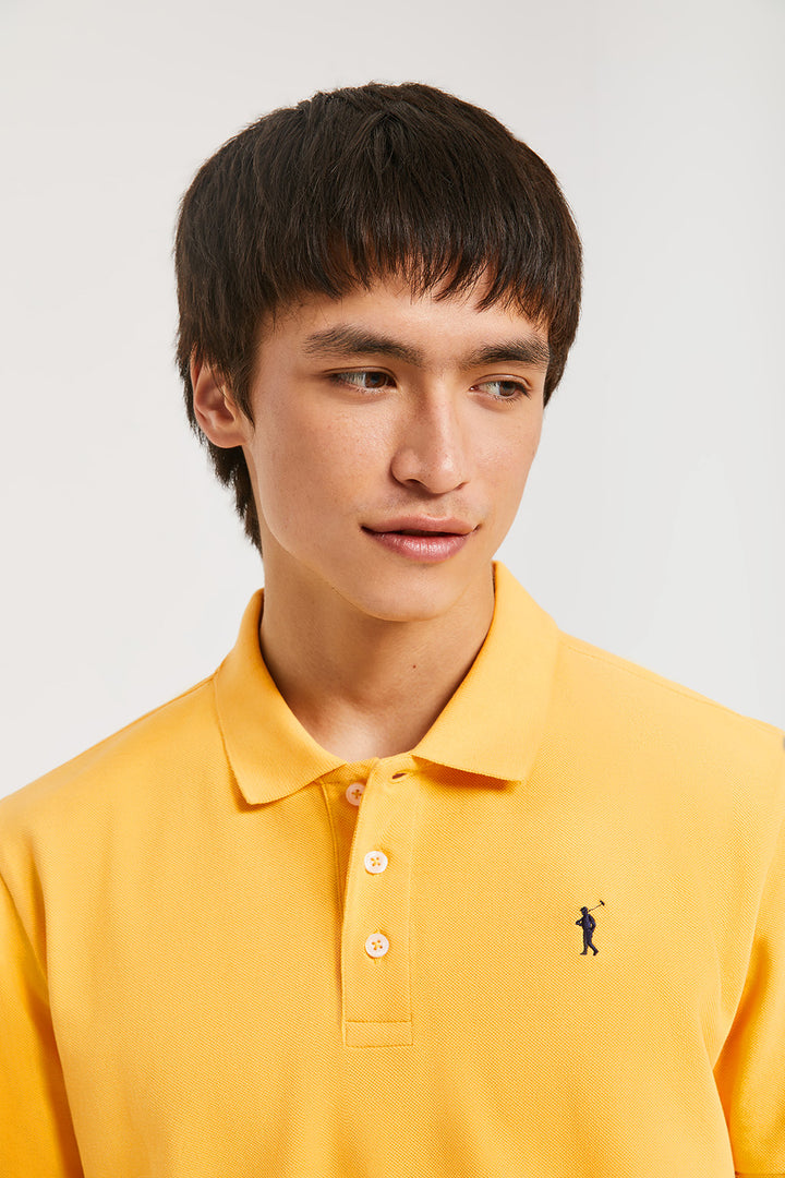 Polo piqué color ambar con tapeta de tres botones y logo bordado en contraste